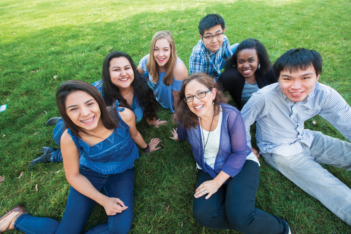 Diverse group of seven students seated on grass and smiling to camera.